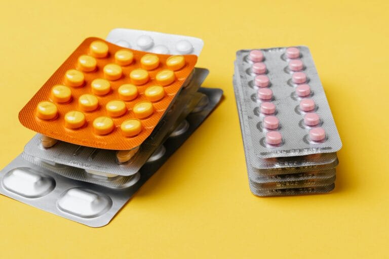 Close-up view of assorted blister packs of pills on a bright yellow background.